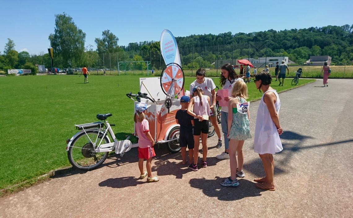 Kinder stehen Schlange vorm Glücksrad bei einem Fußballfeld.