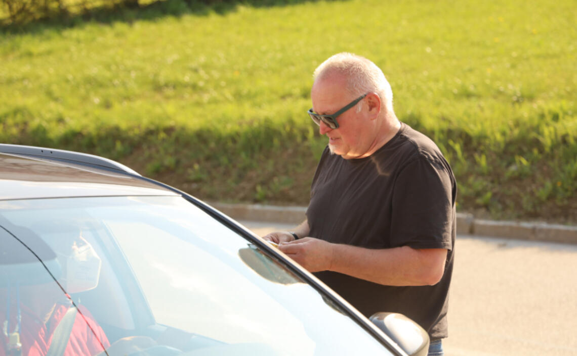 Herr redet mit Person im Auto durch das offene Fenster der Fahrerseite