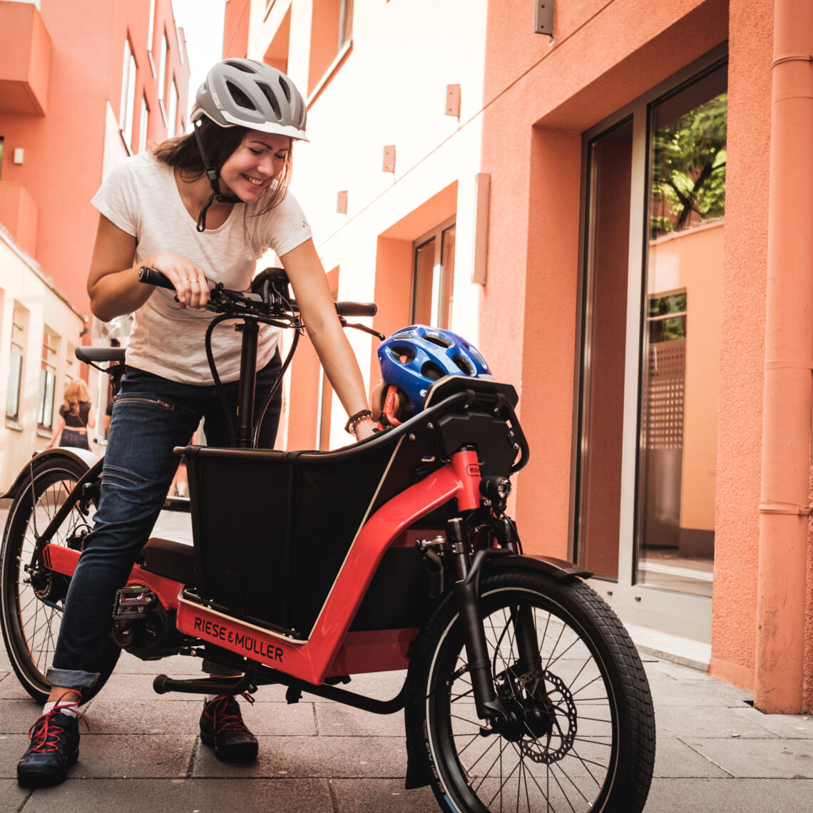 Dame steht mit Lasten-Fahrrad Riese und Müller und redet mit Kind, welches vorne im Korb sitzt