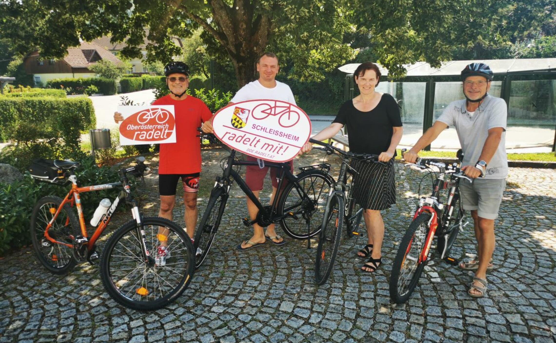 4 Erwachsene stehen mit dem Fahrrad und präsentieren Tafeln 