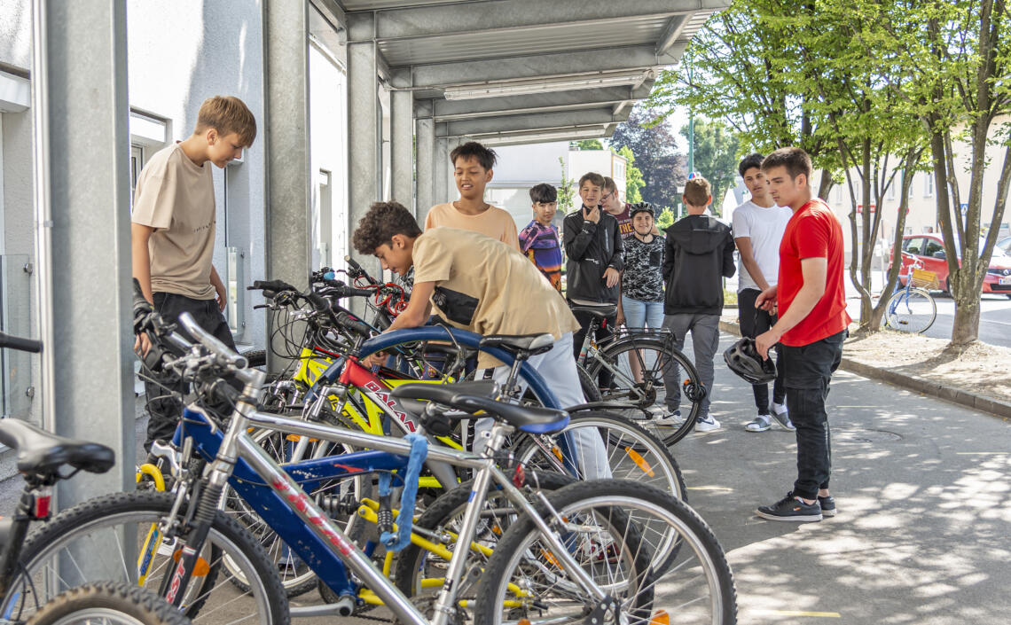Gruppe von Schüler schließen ihre Fahrräder bei einem überdachten Fahrradplatz ab.