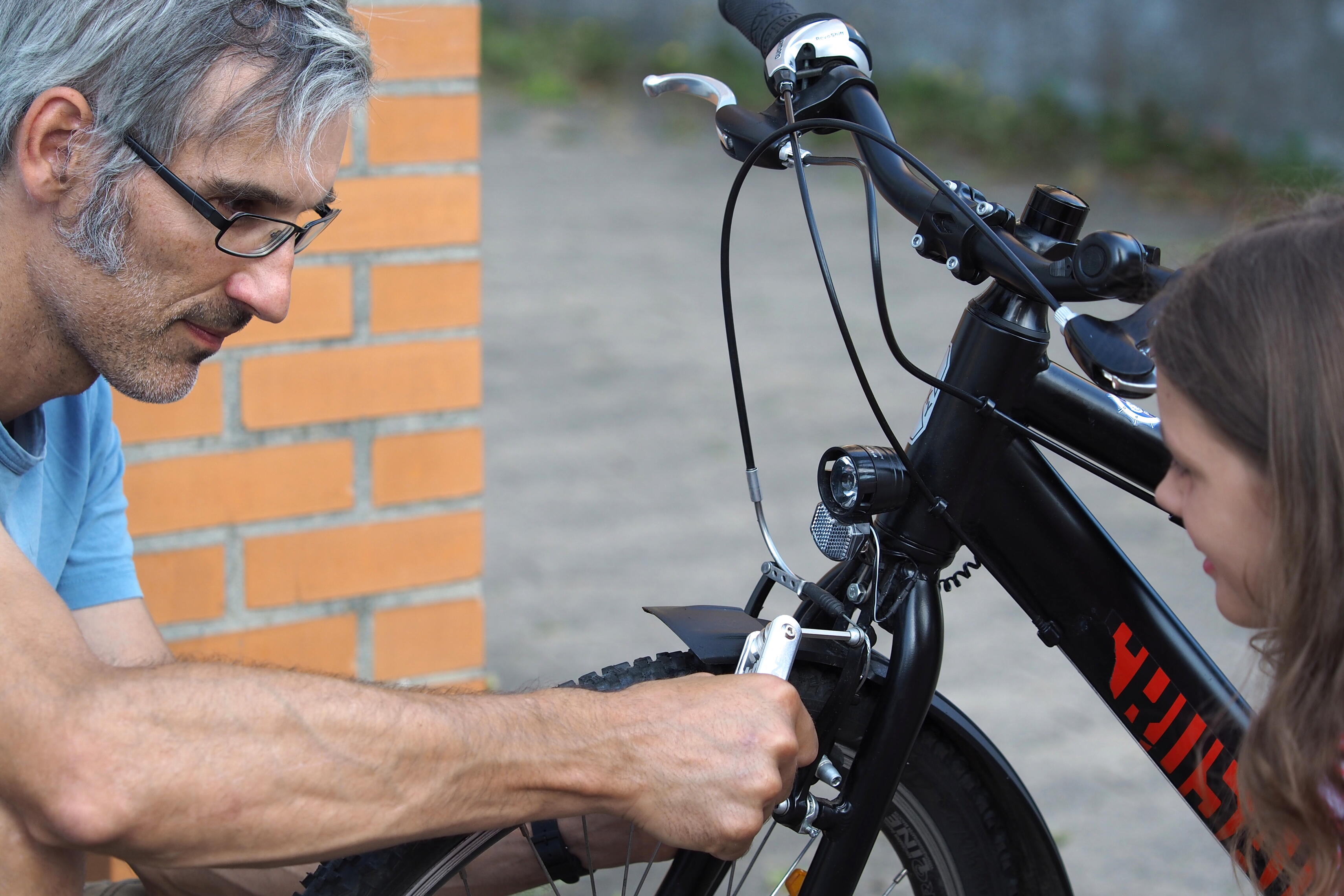 Vater zeigt Tochter, wie man beim Fahrrad die Bremsen nachstellt.