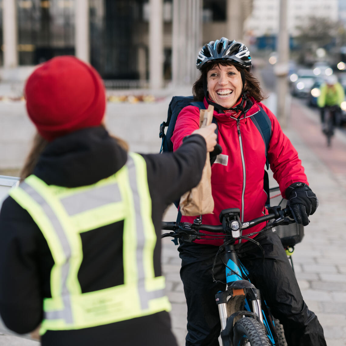 Danke fürs Radfahren; Dame verteilt Frühstücks-sackerl an Fahrradfahrer:innen
