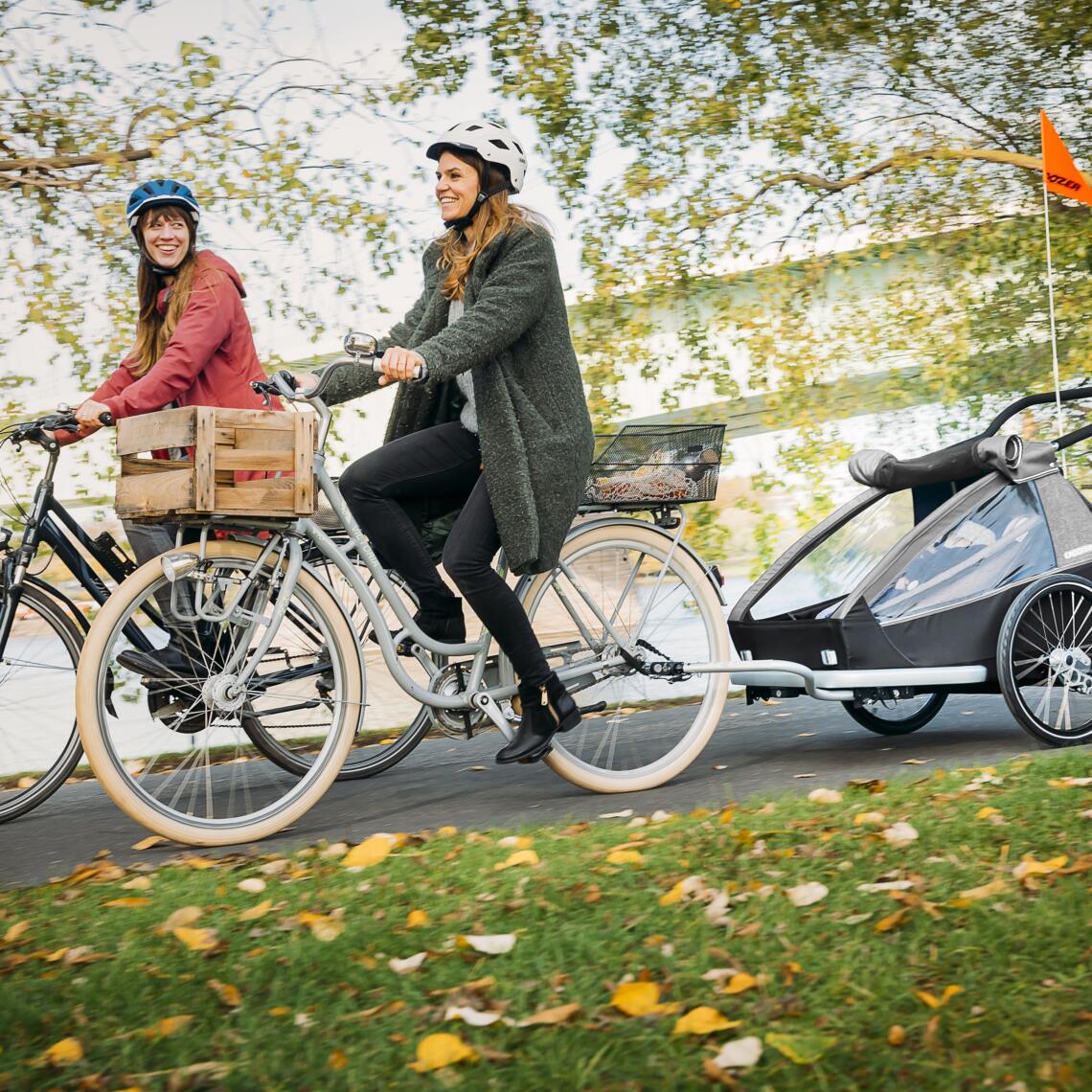 Frauen radeln mit Kinder-Fahrradanhänger im Herbst