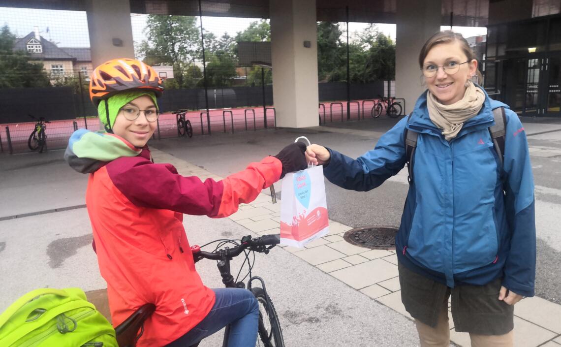 Schüler der BRG Wallererstraße sitzt am Rad und erhält Danke-Sackerl von Pädagogin überreicht