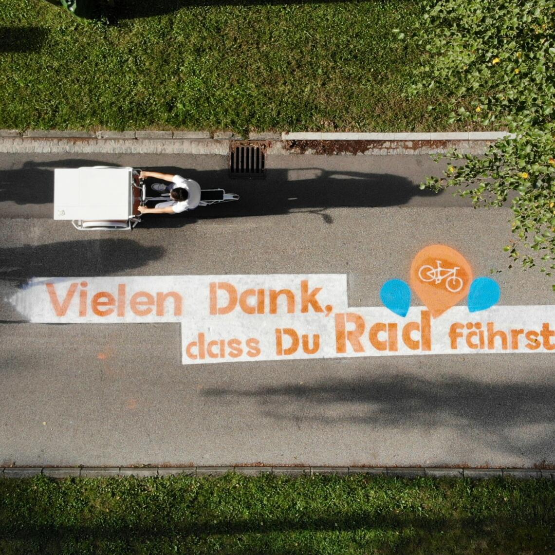 Schriftzug "Vielen Dank, dass du Rad fährst" am Traunradweg in Wels aus der Vogelperspektive mit 3 Radfahrer:innen