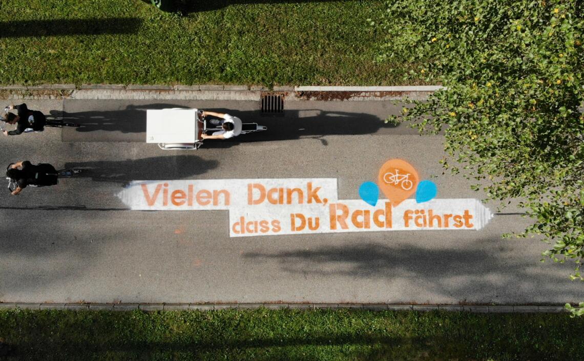 Schriftzug "Vielen Dank, dass du Rad fährst" am Traunradweg in Wels aus der Vogelperspektive mit 3 Radfahrer:innen