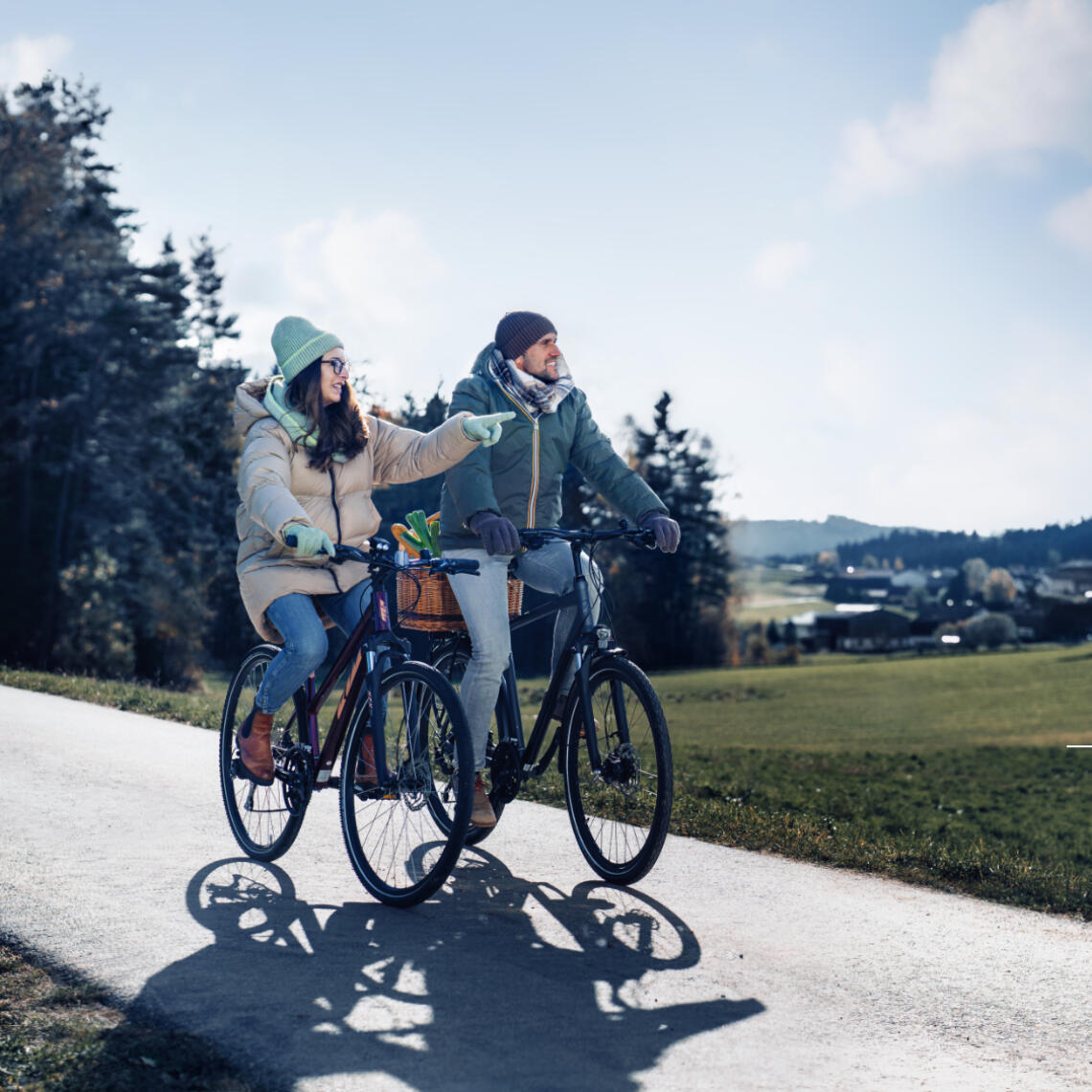 Paar fährt mit Fahrrad aus dem Wald. Beide tragen Wintermäntel und Handschuhe.