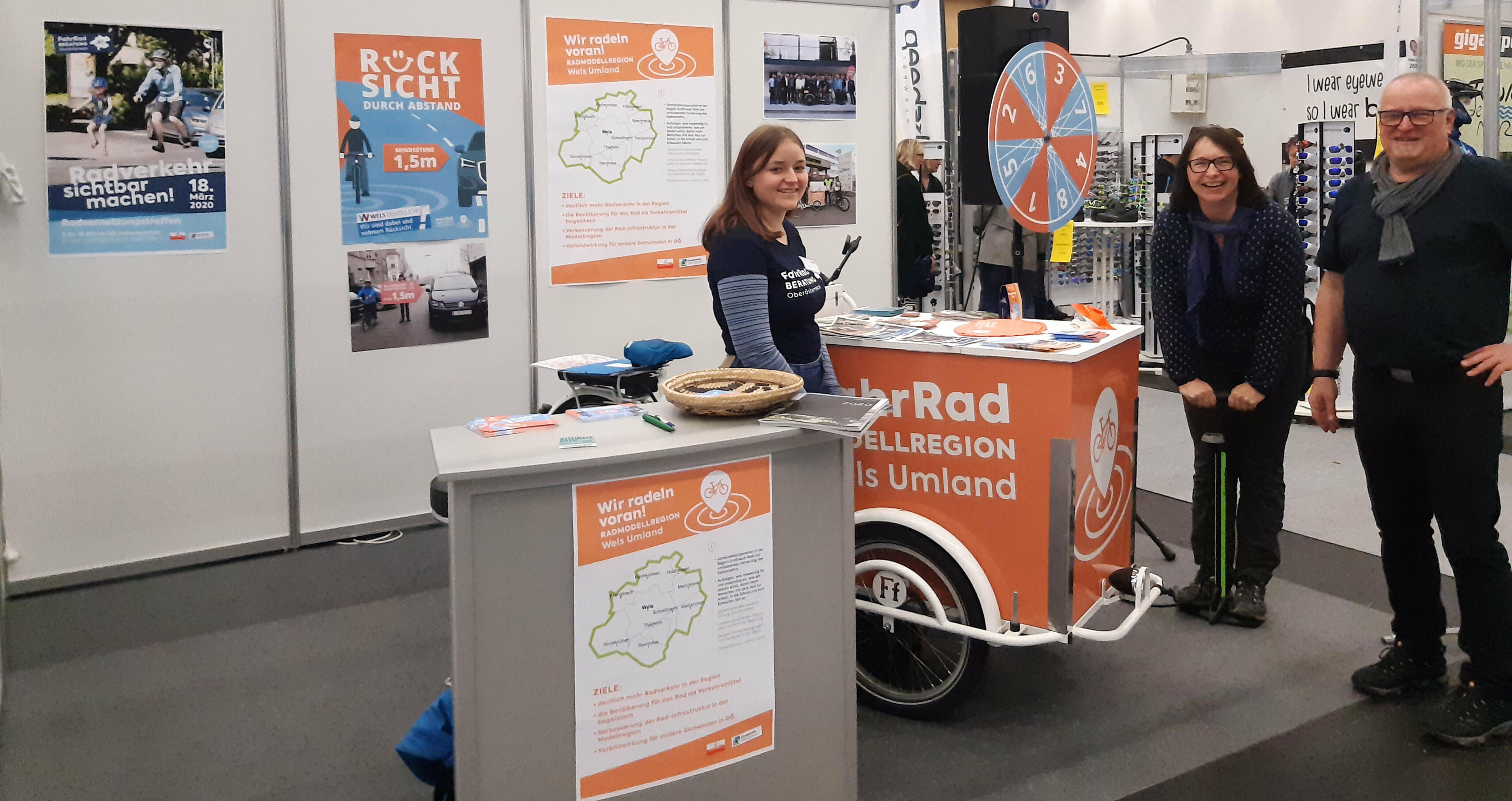 2 Damen und 1 Herr stehen beim Lastenrad mit Glücksrad beim Infostand.