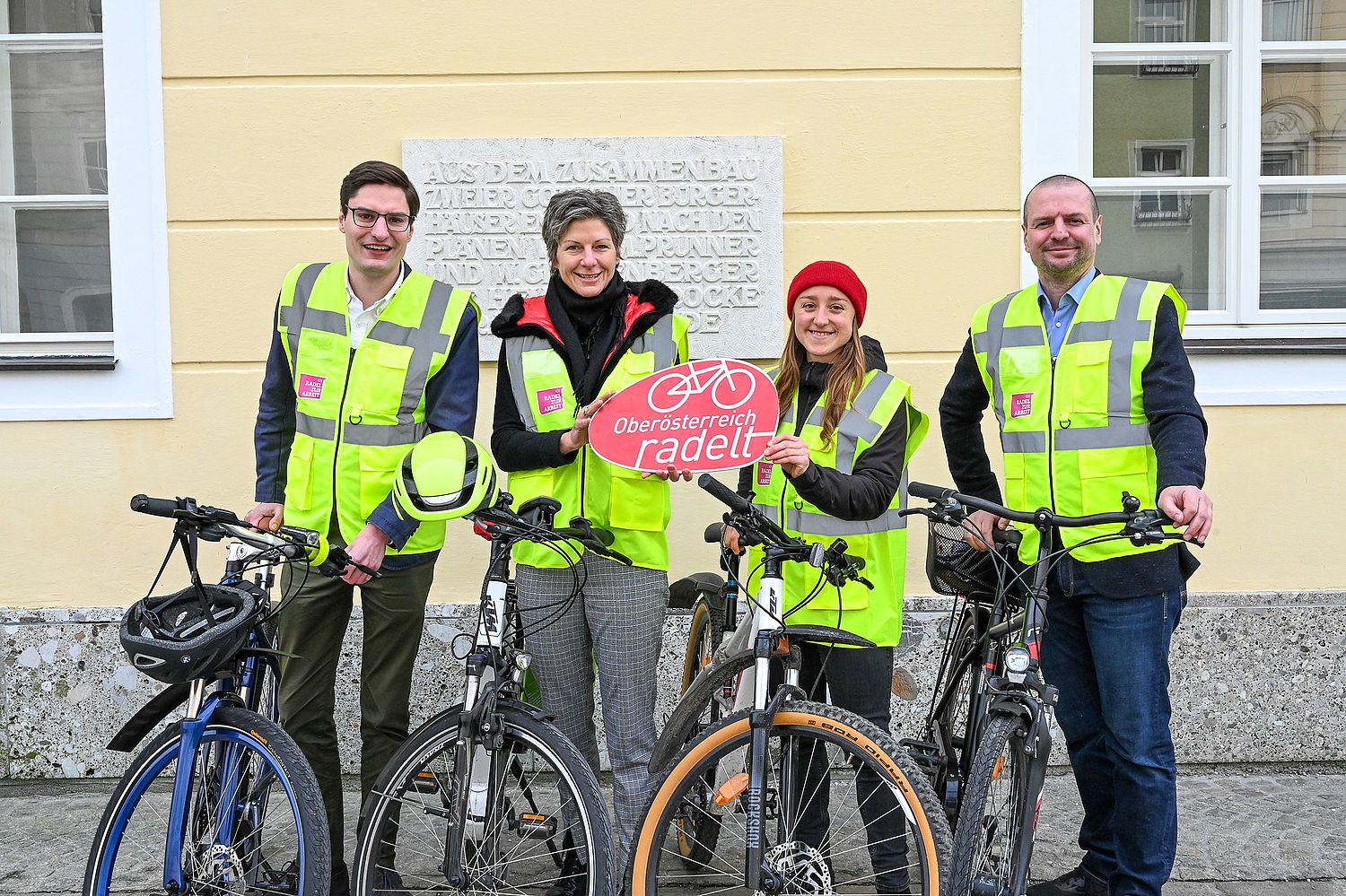 4 Personen mit Fahrrad und Warnweste präsentieren Tafel 