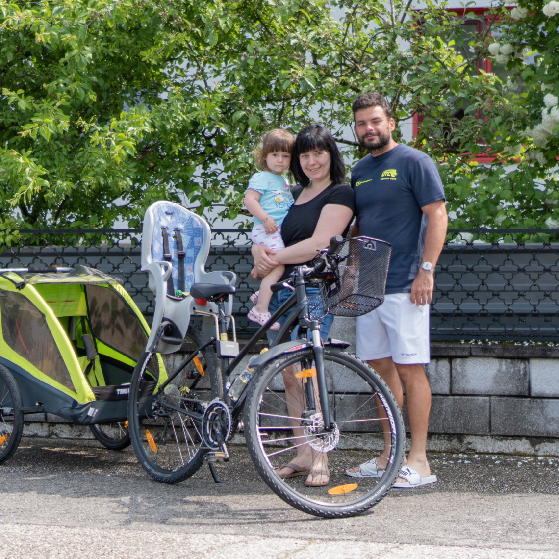 Familie steht vor Fahrrad mit Kinderanhänger und Kindersitz
