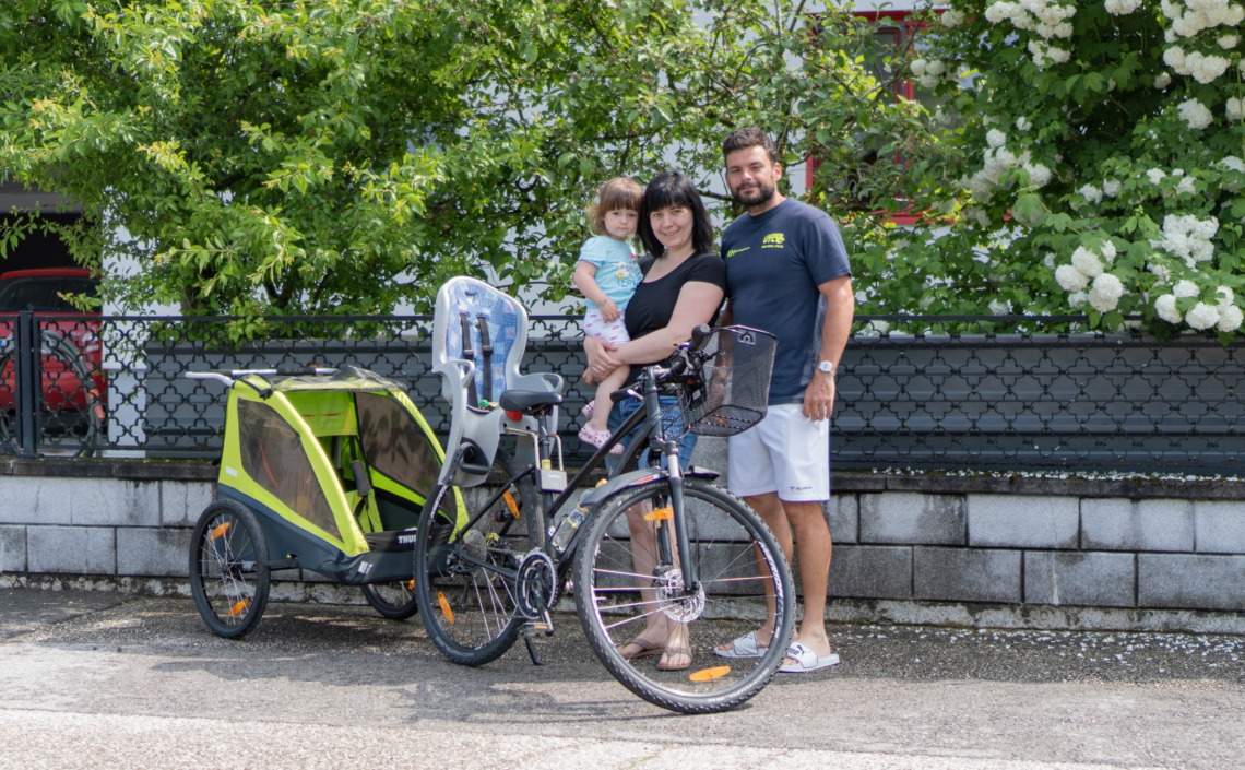 Familie steht vor Fahrrad mit Kinderanhänger und Kindersitz