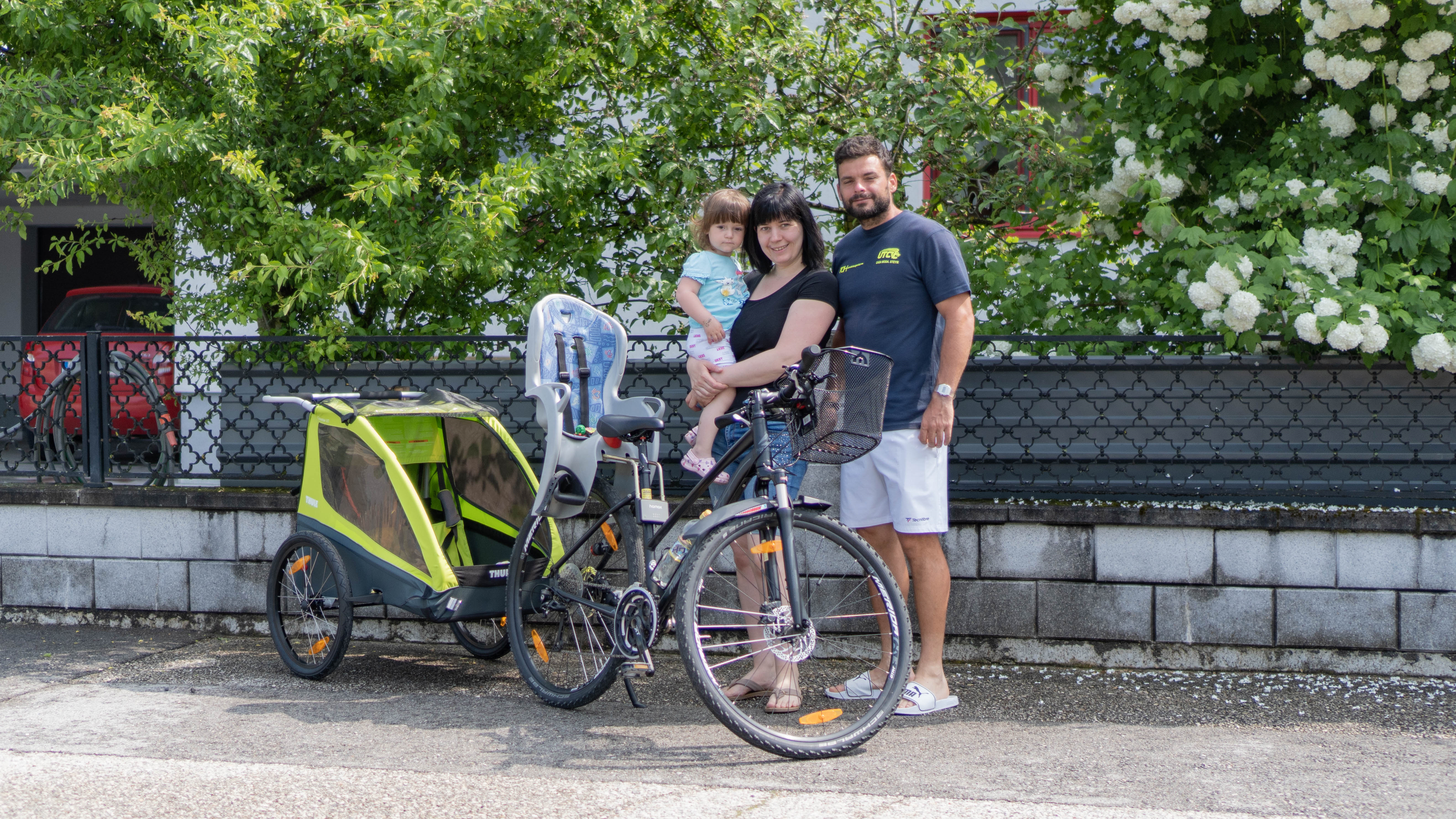 Familie steht vor Fahrrad mit Kinderanhänger und Kindersitz