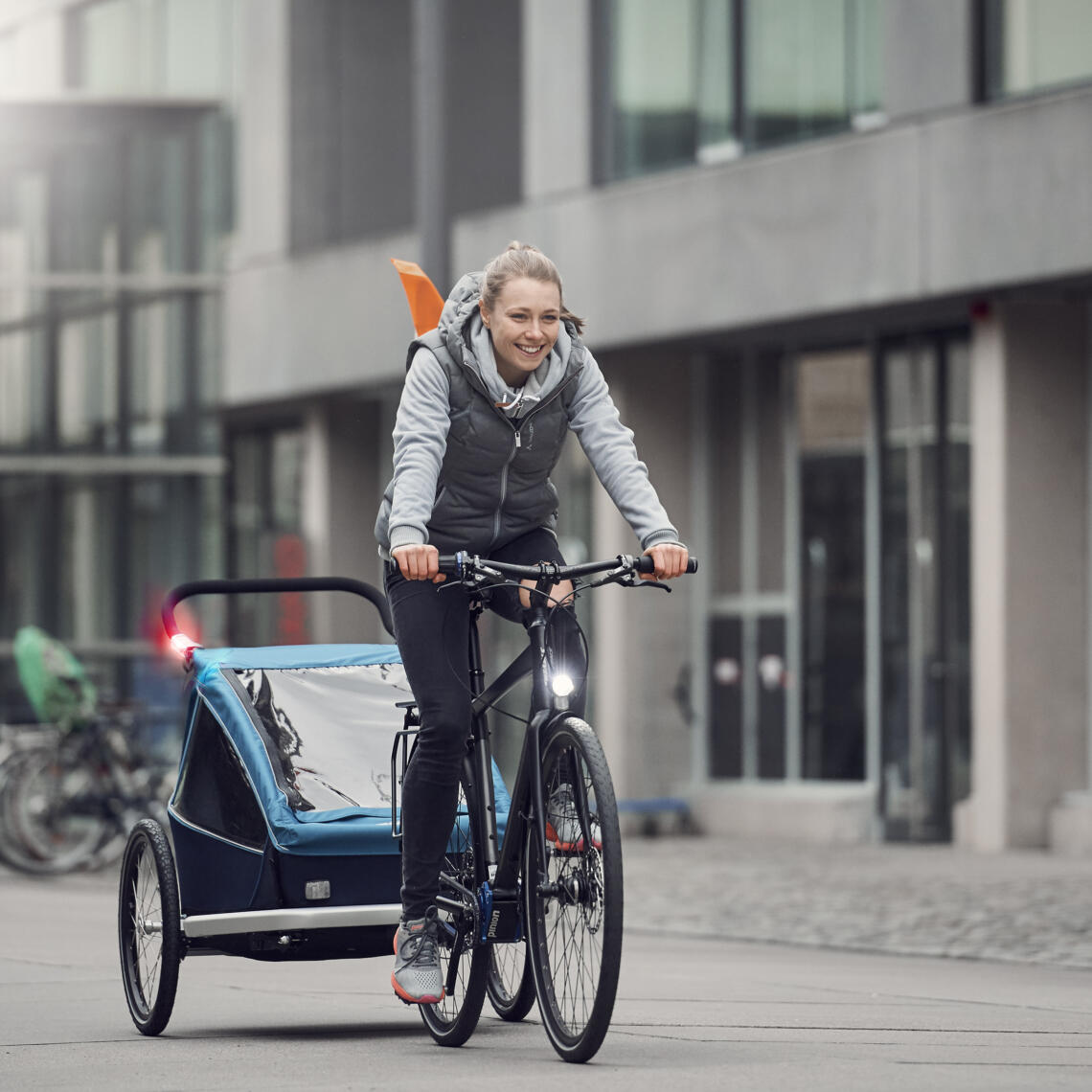 Dame fährt mit Fahrrad und Kinderanhänger durch die Stadt.