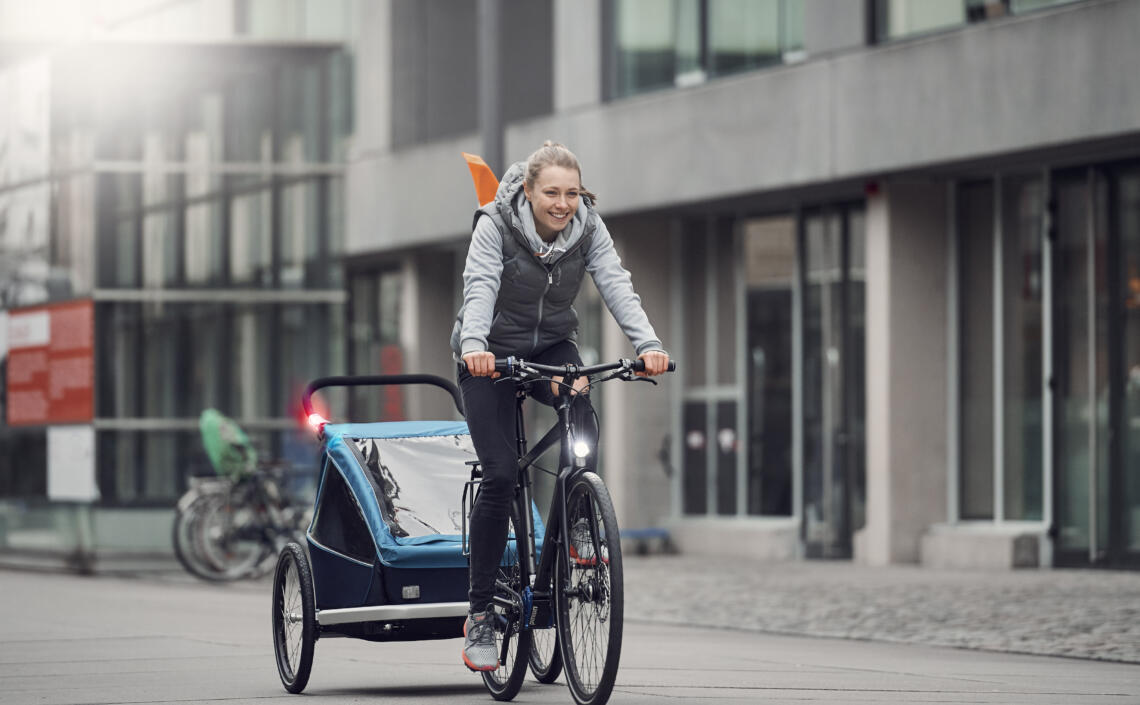 Dame fährt mit Fahrrad und Kinderanhänger durch die Stadt.