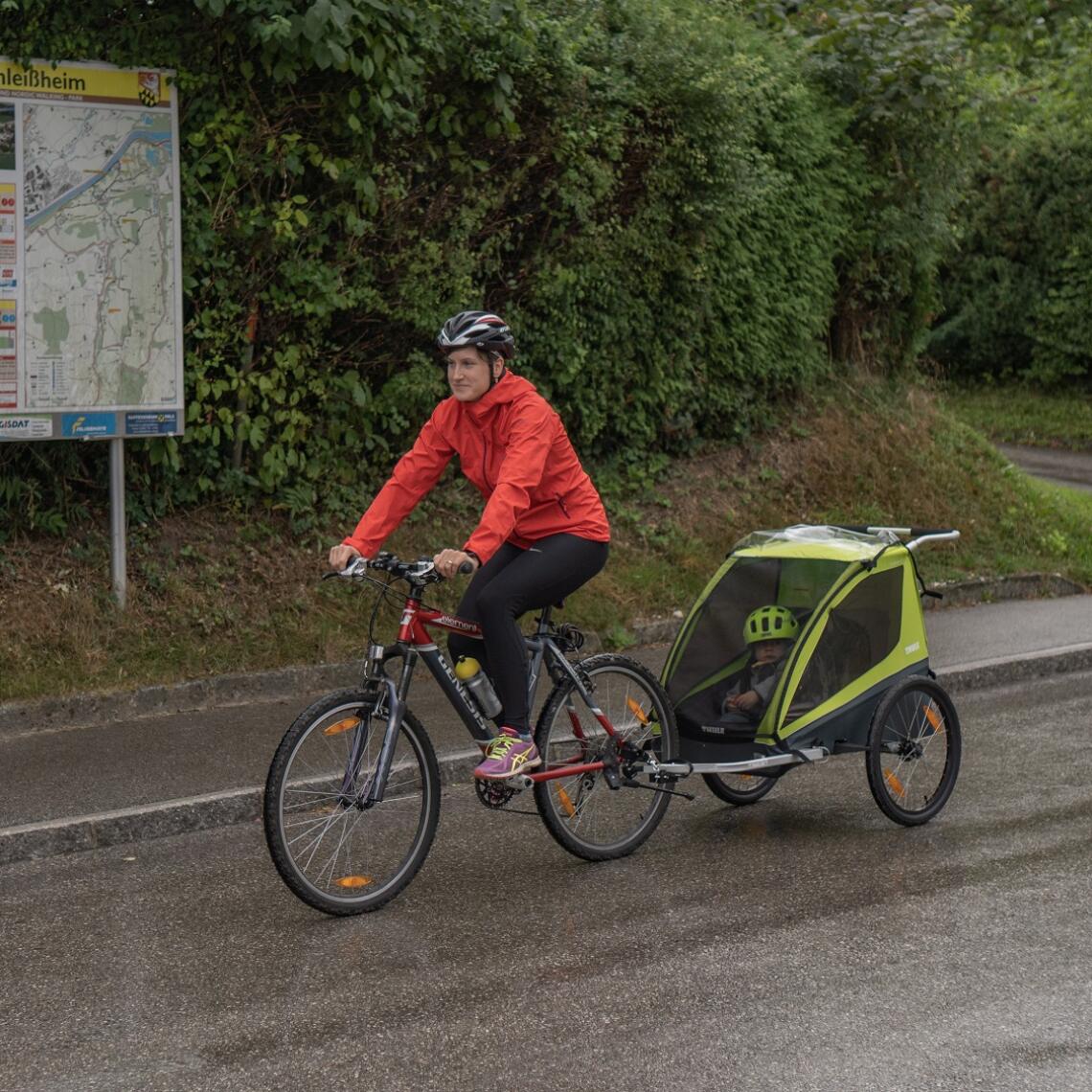 Radfahrerin fährt mit Kinderradanhänger vor Radwegekarte in Schleißheim vorbei