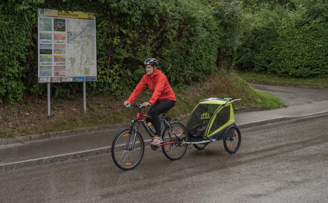Radfahrerin fährt mit Kinderradanhänger vor Radwegekarte in Schleißheim vorbei