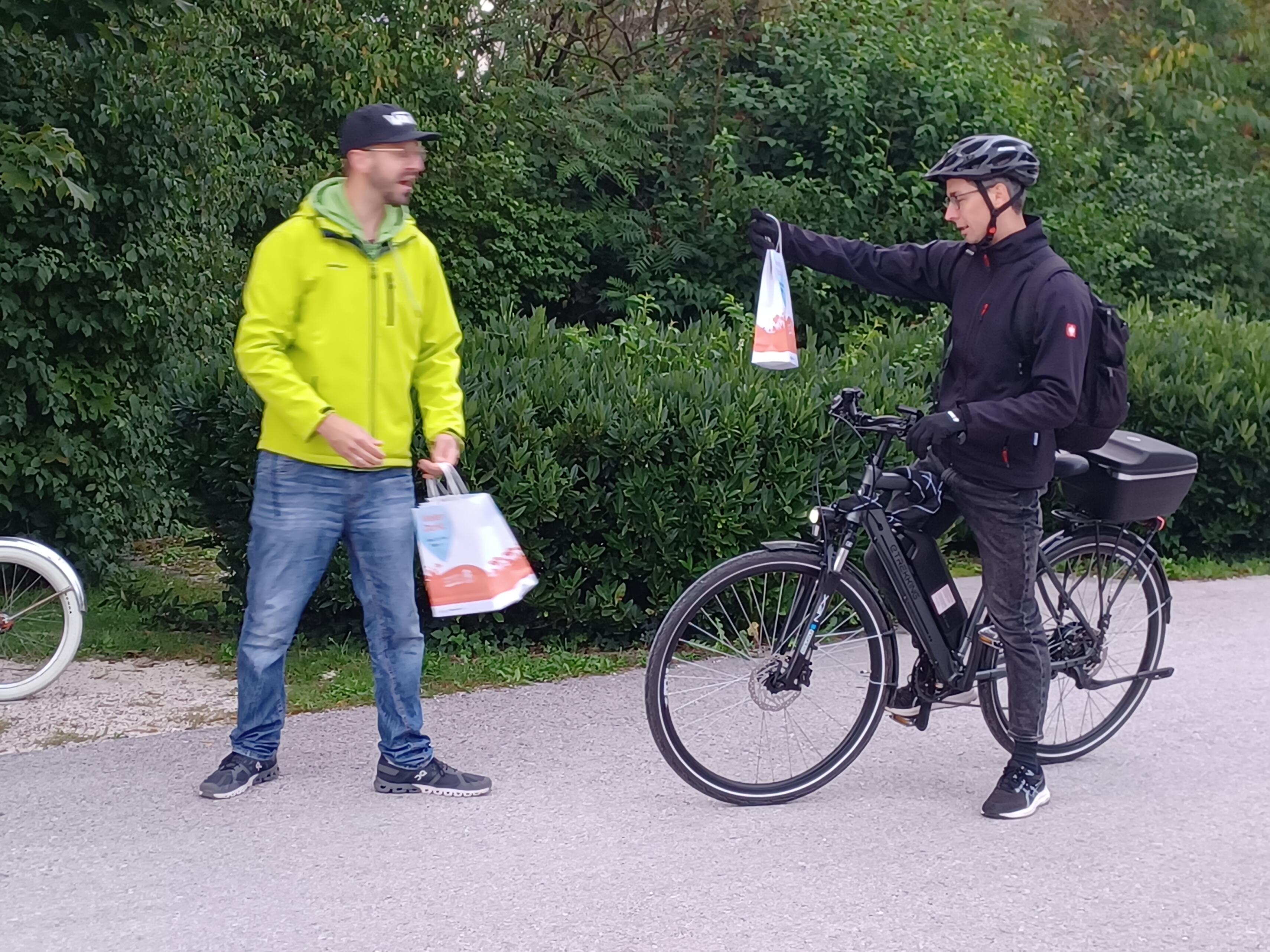 Herr gibt Danke-Sackerl einem Herrn auf dem Fahrrad