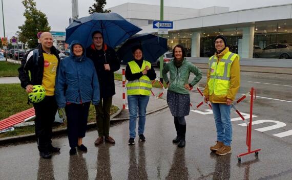 Gruppe fröhlicher Menschen im Regen vor Sperrgitter