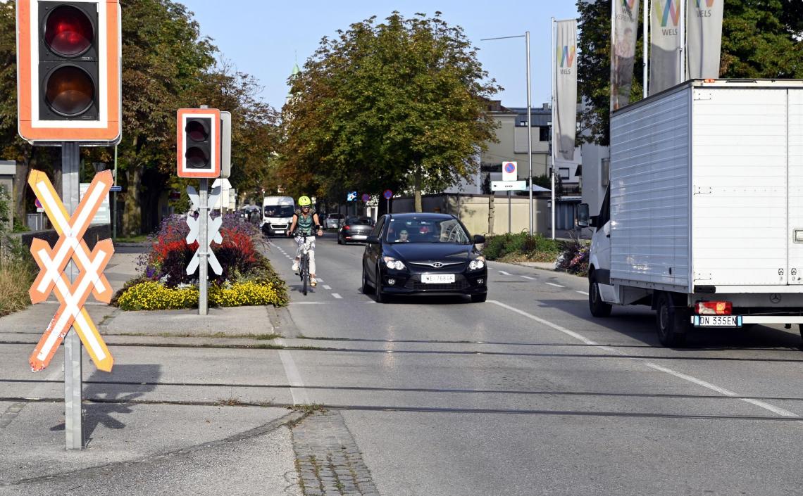 Frau auf Fahrrad wird von Auto überholt bei Bahngleise