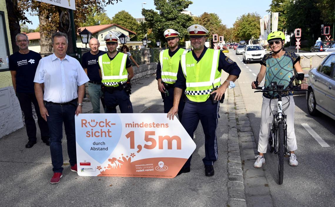 Frau auf Fahrrad und Männer mit Rücksicht durch Abstand Schild