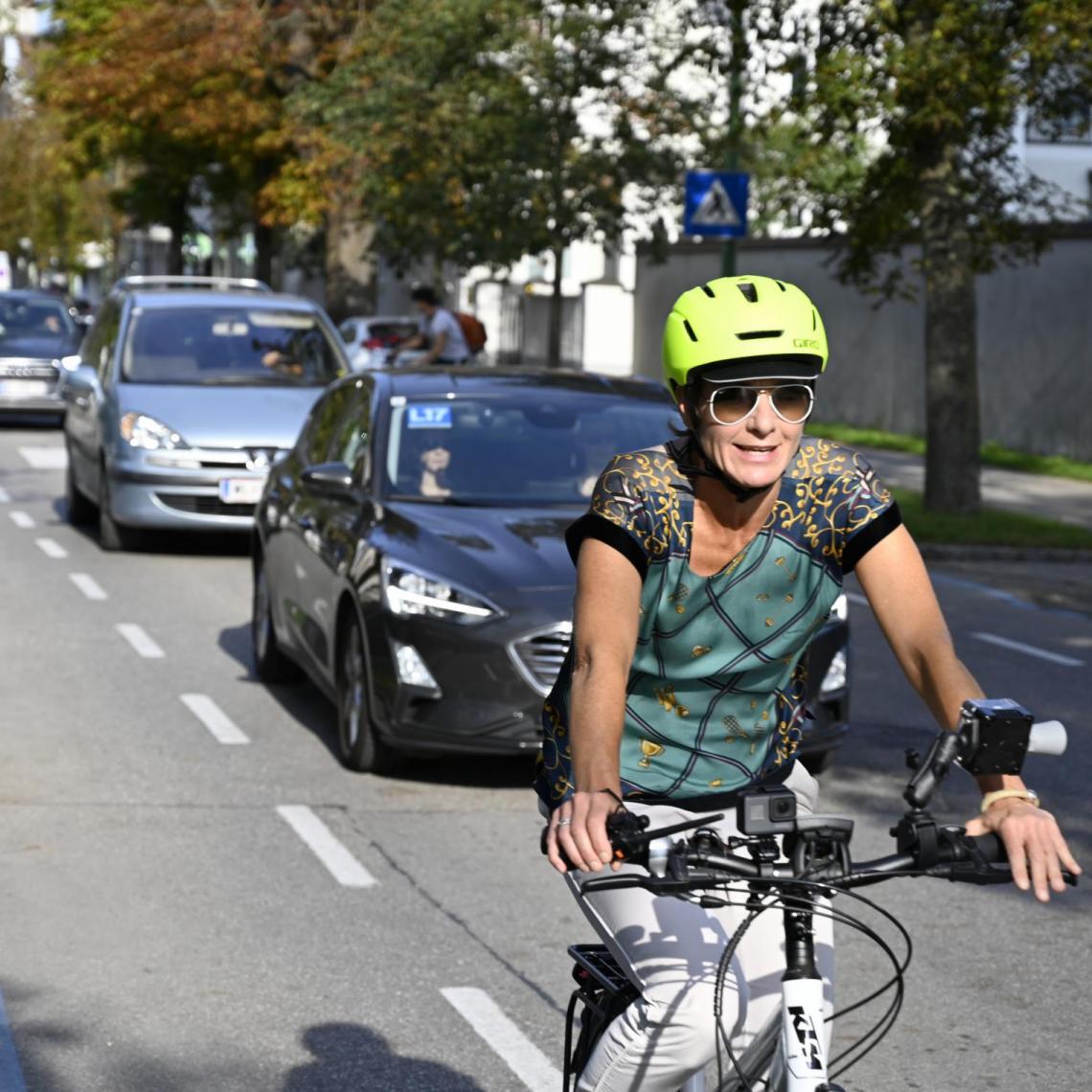 Frau auf Fahrrad, hinter ihr eine Schlange an Autofahrer