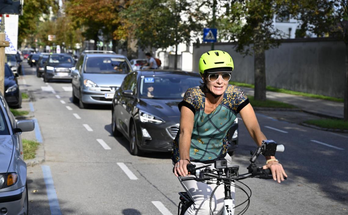 Frau auf Fahrrad, hinter ihr eine Schlange an Autofahrer