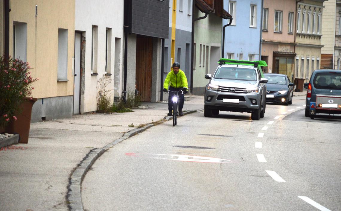 Mann auf Fahrrad wird von Auto überholt