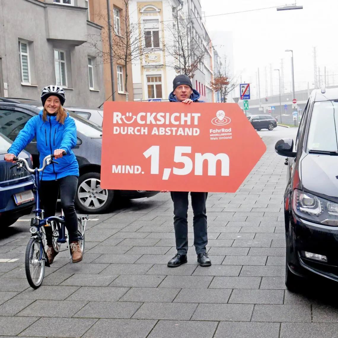 Frau auf Fahrrad und Mann mit Rücksicht durch Abstand Schild